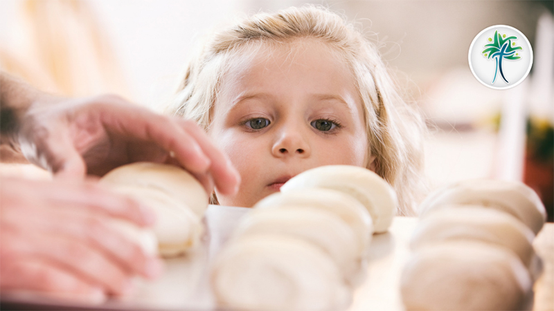 A child looks on as an older person bakes bread.
