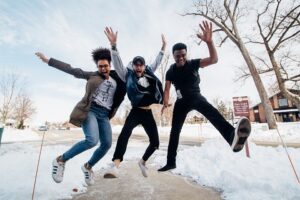 Three young adults or teens from diverse backgrounds leap into the air, smiling.