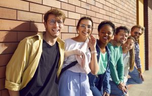 Diverse group of happy, beautiful friends gather together and have fun on city streets. Cheerful, young, multiethnic people in modern, casual wear posing near a brick wall on a sunny day in the summer